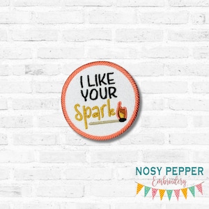 Puede incluir: Parche bordado con el texto "I LIKE YOUR Spark" en negro y dorado, con una ilustración de cerilla y llama. El parche tiene un fondo blanco, un borde naranja y es de forma redonda.