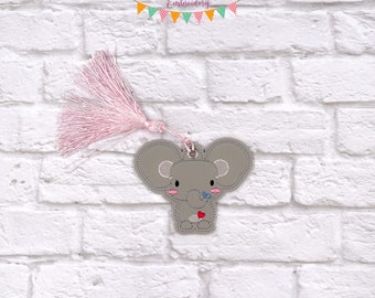 May include: A gray embroidered elephant bookmark with a pink tassel. The elephant is holding a red heart and a blue butterfly.