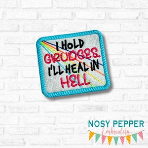 Może przedstawiać: Haftowana naszywka z napisem "I HOLD GRUDGES. I'LL HEAL IN HELL" w kolorze czarnym i różowym. Naszywka ma jasnoniebieską obwódkę i tęczowe linie. Naszywka jest kwadratowa.