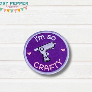 May include: Purple round embroidered patch with a white glue gun and the text "I'm so crafty" in white with two pink hearts.