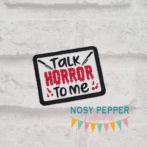 May include: White embroidered patch with black stitching and red text that says "Talk Horror To Me" with a knife graphic. The patch is on a white brick background.