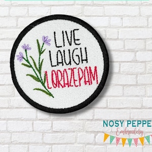 May include: Round embroidered patch with a white background, black border, and the words "LIVE LAUGH LORAZEPAM" in black and red. A floral design with purple flowers and green stems is on the left. The patch is circular.