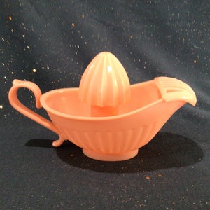 May include: A pink plastic citrus juicer with a ribbed design. The juicer has a spout and a handle.