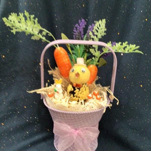 May include: A pink metal basket with a handle, filled with straw, carrots, and a small yellow chick figurine. The basket is decorated with a pink ribbon.