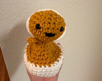 May include: A crocheted plush toy in the shape of a person with a brown body and a white crocheted hat. The toy has black eyes and a smiling mouth.