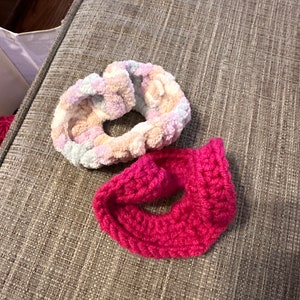Puede incluir: Dos scrunchies de pelo de ganchillo. Uno es rosa y el otro es una mezcla pastel de rosa, azul y blanco.