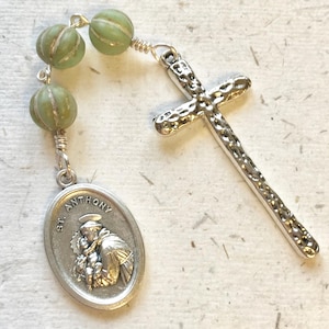 May include: A silver rosary with green beads and a silver cross. The centrepiece features a silver oval medallion with the image of Saint Anthony and the text "St. Anthony".