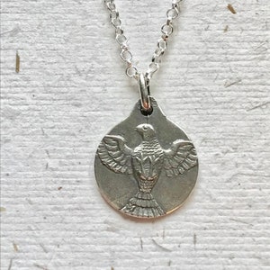 May include: A silver necklace with a pendant featuring a detailed, embossed dove design. The dove is depicted with its wings spread, symbolising peace and hope.