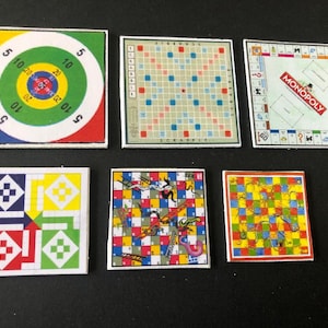 May include: Set of miniature board games, including a red, yellow, green, and blue target game, a Scrabble board, a Monopoly board, a red, yellow, green, and blue checkerboard game, a Snakes and Ladders board, and a Chutes and Ladders board.