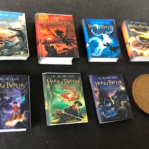 May include: Set of seven miniature Harry Potter books with colourful covers featuring illustrations from the series. The books are arranged in two rows, with a copper-coloured coin in the bottom right corner.