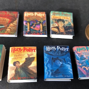 Può includere: Un set di sette libri in miniatura con copertina rigida che presentano le copertine della serie di Harry Potter. I libri sono disposti su due file, con la prima fila che presenta le copertine di "Harry Potter e la pietra filosofale", "Harry Potter e la camera dei segreti" e "Harry Potter e il prigioniero di Azkaban". La seconda fila presenta le copertine di "Harry Potter e il calice di fuoco", "Harry Potter e l'Ordine della Fenice", "Harry Potter e il principe mezzosangue" e "Harry Potter e i Doni della Morte".