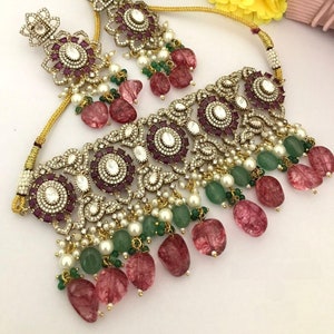 May include: An ornate necklace and earring set. The jewelry features a gold-colored chain and setting, with a floral design. The necklace and earrings are adorned with clear and ruby-colored stones, white pearls, and green and pink beads.