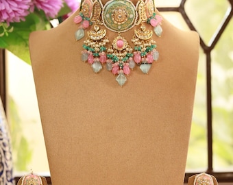 May include: An ornate necklace and matching earrings set displayed on a mannequin. The jewelry features a gold-tone base with pink, green, and blue gemstones. The necklace is a choker style, and the earrings are dangling.