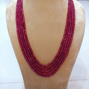 May include: A multi-strand necklace made of deep red gemstone beads. The necklace is displayed on a mannequin bust.