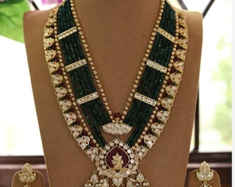 May include: A multi-strand necklace with a large pendant featuring a deity figure. The necklace is made of green beads, gold, and red stones. Matching earrings are also included.
