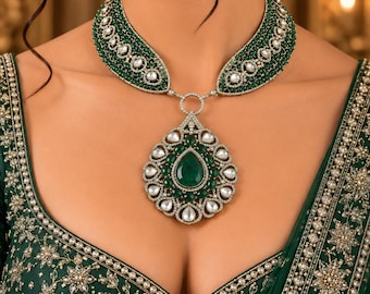 May include: A jewellery set featuring a necklace and matching earrings. The necklace has a large, teardrop-shaped pendant with a central green stone surrounded by white stones, suspended from a wide band of green and white beads. Matching earrings.