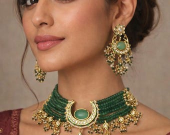May include: A woman wearing a gold necklace and earring set. The necklace has a crescent-shaped pendant with a green stone and multiple strands of green beads. The earrings have a similar design with green stones and dangling beads.
