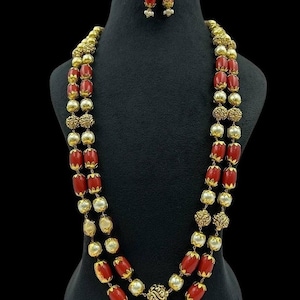 May include: A two-strand necklace and earrings set featuring red and white beads. The necklace has a gold-toned clasp and the earrings have gold-toned hooks.