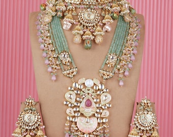 May include: A detailed gold-coloured jewellery set comprising a choker, long necklace, and earrings. The set features intricate designs with pearls, pink and green beads, and a large pendant with a pink gemstone. The jewellery is displayed on a mannequin.
