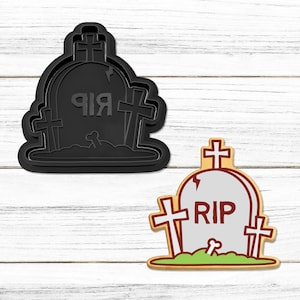 Może przedstawiać: Czarna plastikowa foremka do ciasteczek w kształcie nagrobka z krzyżem na górze i napisem "RIP" z przodu. Obok foremki znajduje się brązowe ciasteczko o podobnym wzorze.