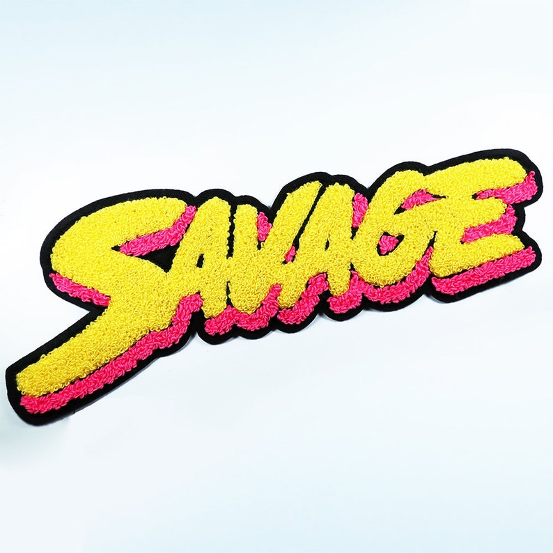 May include: A yellow and pink embroidered patch with the word "SAVAGE" in a bold, stylised font.
