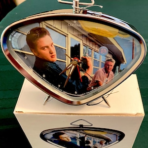May include: A silver-colored alarm clock with a retro design. The clock face features a picture of Elvis Presley and the text "Centric".