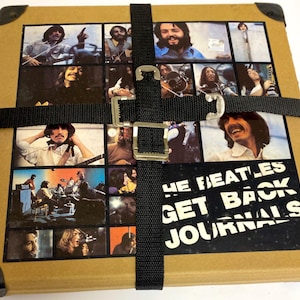 May include: A brown cardboard box with a black strap and buckle. The box has a collage of photos of the Beatles on the front with the text "The Beatles Get Back Journals".