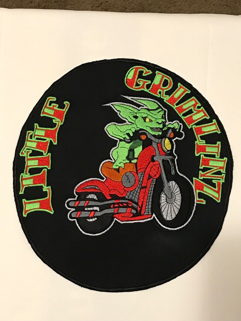 K&ouml;nnte beinhalten: Ein gestickter schwarzer und roter Aufn&auml;her mit einem gr&uuml;nen Kobold, der ein Motorrad f&auml;hrt. Der Aufn&auml;her zeigt links "Little" und rechts "Grinlinz".