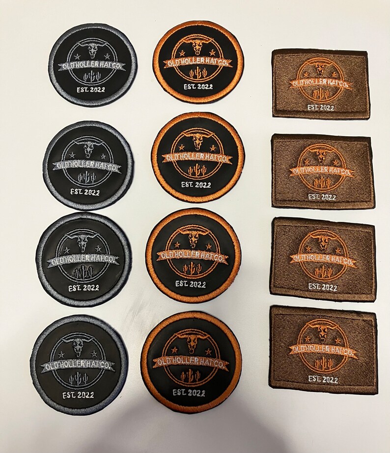K&ouml;nnte beinhalten: Zw&ouml;lf runde und rechteckige Patches mit schwarzem Hintergrund und braunem oder silbernem Rand. Die Patches zeigen einen Sch&auml;del mit H&ouml;rnern, einen Stern und den Text "Old Holler Hat Co. Est. 2022".