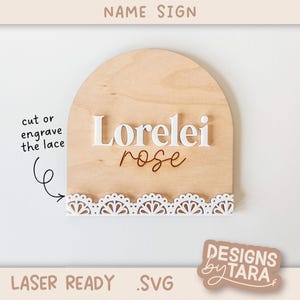 Peut inclure: Panneau de nom en bois avec un dessus en forme d'arche. Le nom "Lorelei" est en blanc, avec "rose" en écriture cursive. Un motif de dentelle blanche est en bas. Le texte "NAME SIGN", "LASER READY .SVG" et "DESIGNS by TARA" sont également visibles.