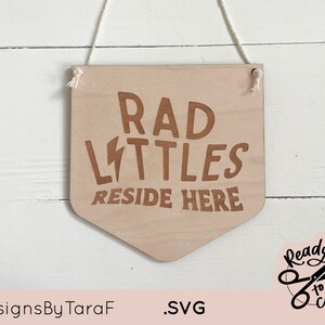 May include: A wooden sign with the text "Rad Littles Reside Here" in brown lettering. The sign is hanging from a white string and has a lightning bolt graphic.