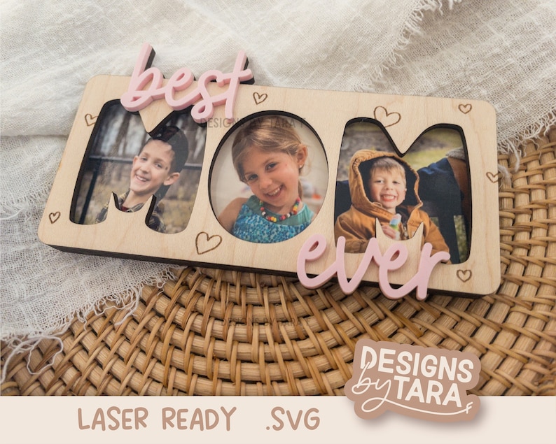May include: Wooden photo frame with the words "best mom ever" in pink lettering. The frame has three cut-out spaces for photos and is decorated with small hearts.