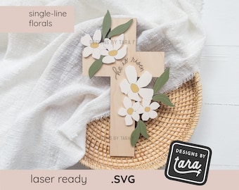 May include: Wooden cross with the text "He is risen" and a floral design with white flowers and green leaves.