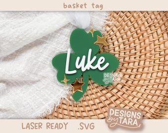 May include: Green shamrock-shaped laser cut basket tag with the name "Luke" in white lettering and gold glitter stars. The tag is on a woven wicker background.