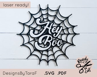 Può includere: Design a taglio laser in bianco e nero di una ragnatela con le parole "Hey Boo" in un font di scrittura bianco. Il design è pronto per essere tagliato con un cutter laser.