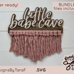 Peut inclure: Panneau en bois avec l'inscription "little babe cave" en écriture blanche. Le panneau a un cadre en bois marron et une frange en macramé rose. Le texte "laser ready!" et "BUNDLE - 3 files included!" sont également visibles.