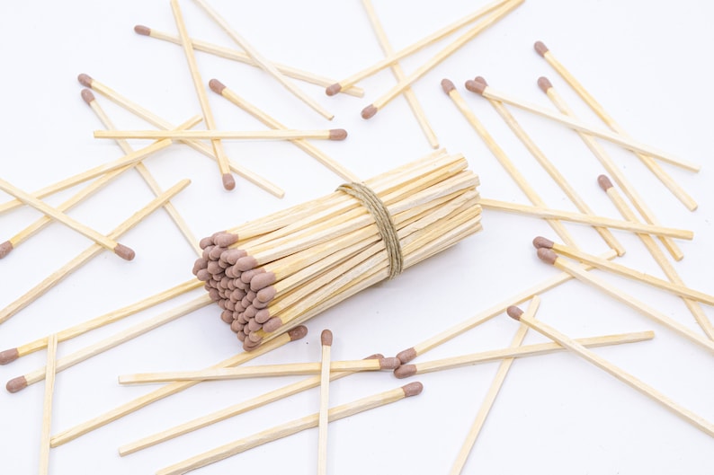 May include: A bundle of wooden matches with brown tips, tied together with twine, surrounded by loose matches on a white surface.