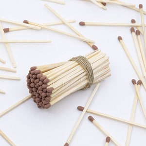 May include: A bundle of wooden matches with brown tips, tied together with twine, surrounded by loose matches on a white surface.