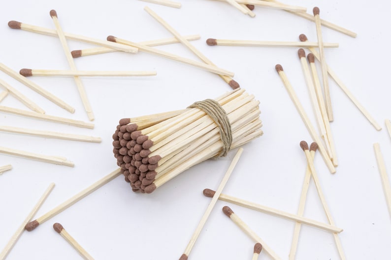 May include: A bundle of wooden matches with brown tips, tied together with twine, surrounded by loose matches on a white surface.