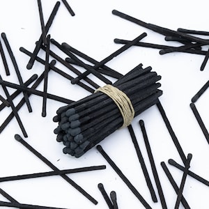 May include: A bundle of black matches tied together with twine, surrounded by loose black matches on a white surface.