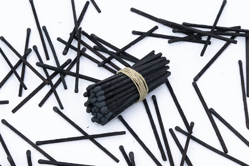 May include: A bundle of black matches tied together with twine, surrounded by loose black matches on a white surface.