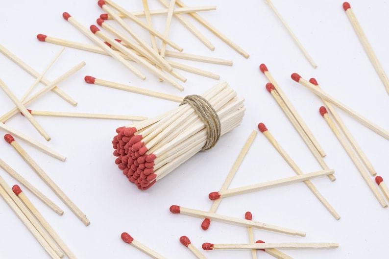 May include: A bundle of red-tipped wooden matches tied together with twine, surrounded by loose matches on a white surface.