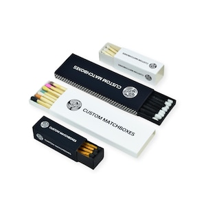 Może przedstawiać: Trzy pudełka zapałek z czarno-białym opakowaniem. Pudełka zapałek mają nadrukowany tekst "Custom Matchboxes". Pudełka zapałek są ułożone po przekątnej od góry po lewej do dołu po prawej.