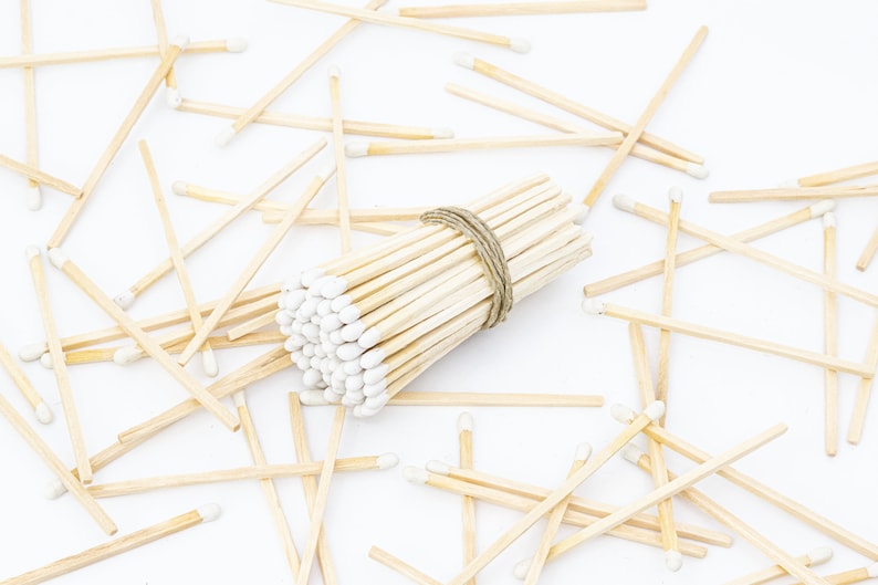 May include: A bundle of white tipped wooden matches tied together with twine, surrounded by loose matches on a white surface.
