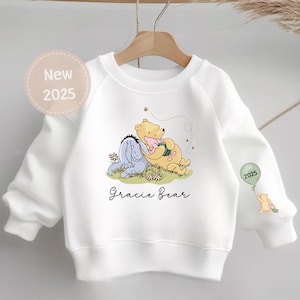 May include: White sweatshirt with a Winnie the Pooh and Piglet graphic, the text "Gracie Bear" and the year "2025" printed on it.