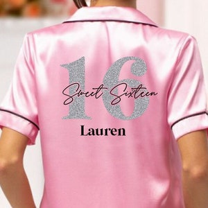 Può includere: Set pigiama in raso rosa con finiture nere. La parte posteriore della parte superiore presenta un "16" argentato glitterato e le parole "Sweet Sixteen" e un nome in nero. Il set include una camicia a maniche corte con bottoni e pantaloncini abbinati.