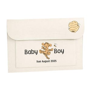 May include: A beige felt folder with a pocket on the front. The pocket has a printed design of a cartoon tiger, two bees, and the text "Baby Boy Due August 2025". The top of the folder has a printed design of a honeycomb with bees.