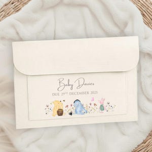 Puede incluir: Sobre crema para anuncio de bebé con cierre de solapa. La parte delantera presenta el texto "Baby Davies DUE 29TH DECEMBER 2025" sobre una ilustración de acuarela de personajes de Winnie the Pooh y flores.