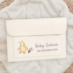 May include: Cream-colored baby announcement envelope featuring a Winnie the Pooh illustration with Piglet. The text reads "Baby Jenkins DUE DECEMBER 2025". The envelope is made of a soft, textured material.