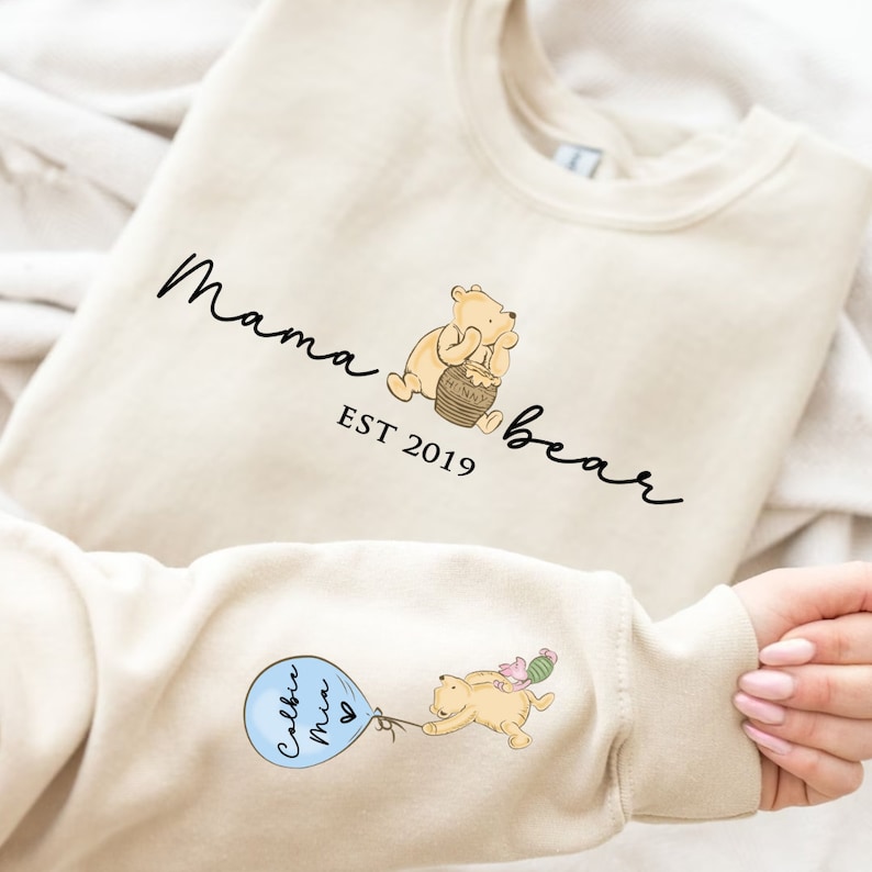 May include: A cream colored sweatshirt with the text "Mama bear est 2019" and a cartoon image of Winnie the Pooh holding a honey pot. The sweatshirt also has a cartoon image of Winnie the Pooh holding a balloon with the text "Callie Mia" on it.